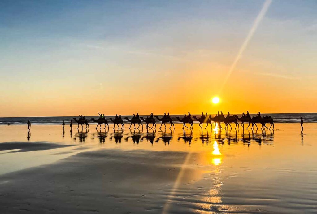 Una lunga fila di cammelli attraversa Cable Beach al tramonto, Australia